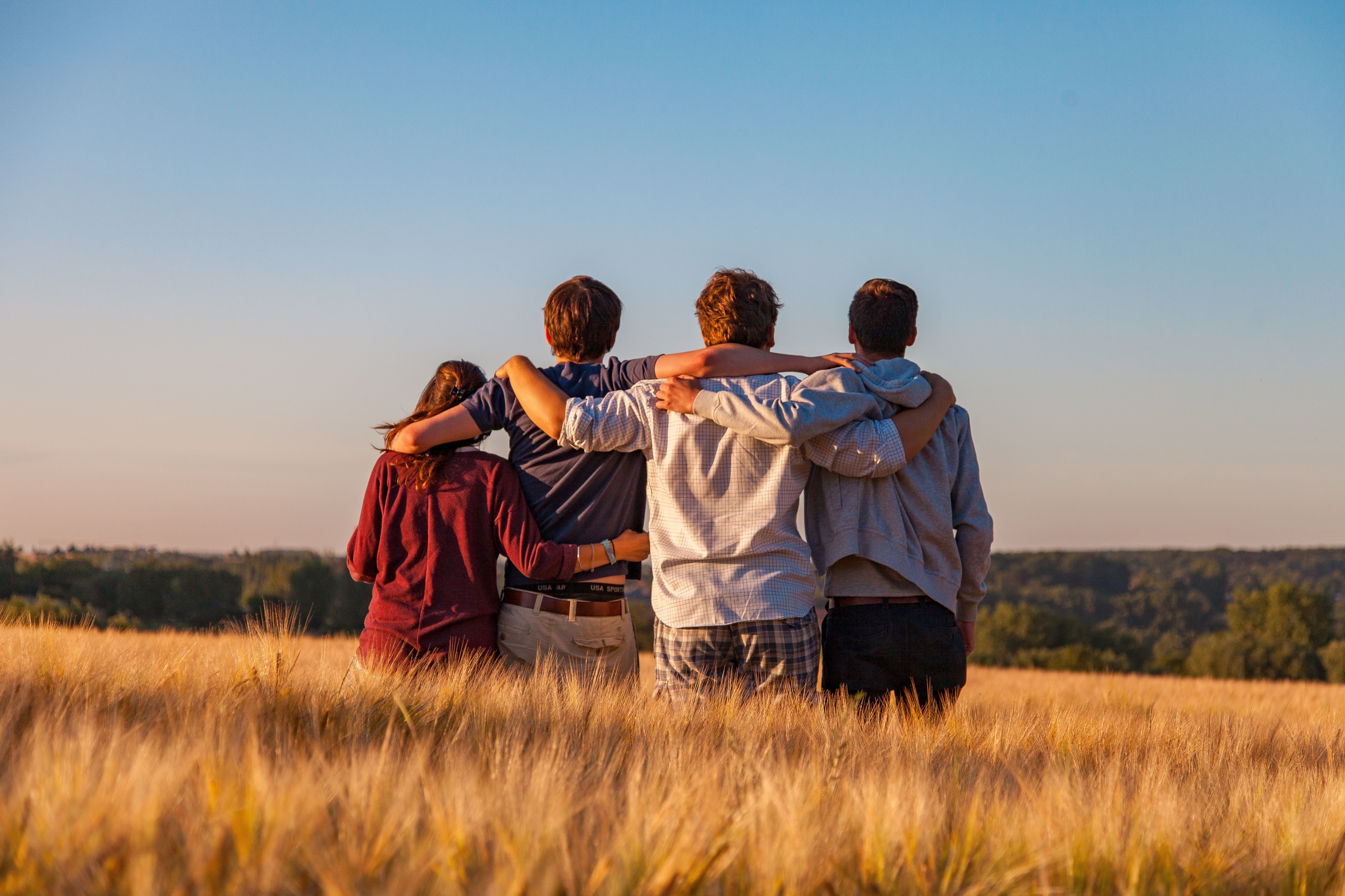 Friends embracing in a field at sunset.