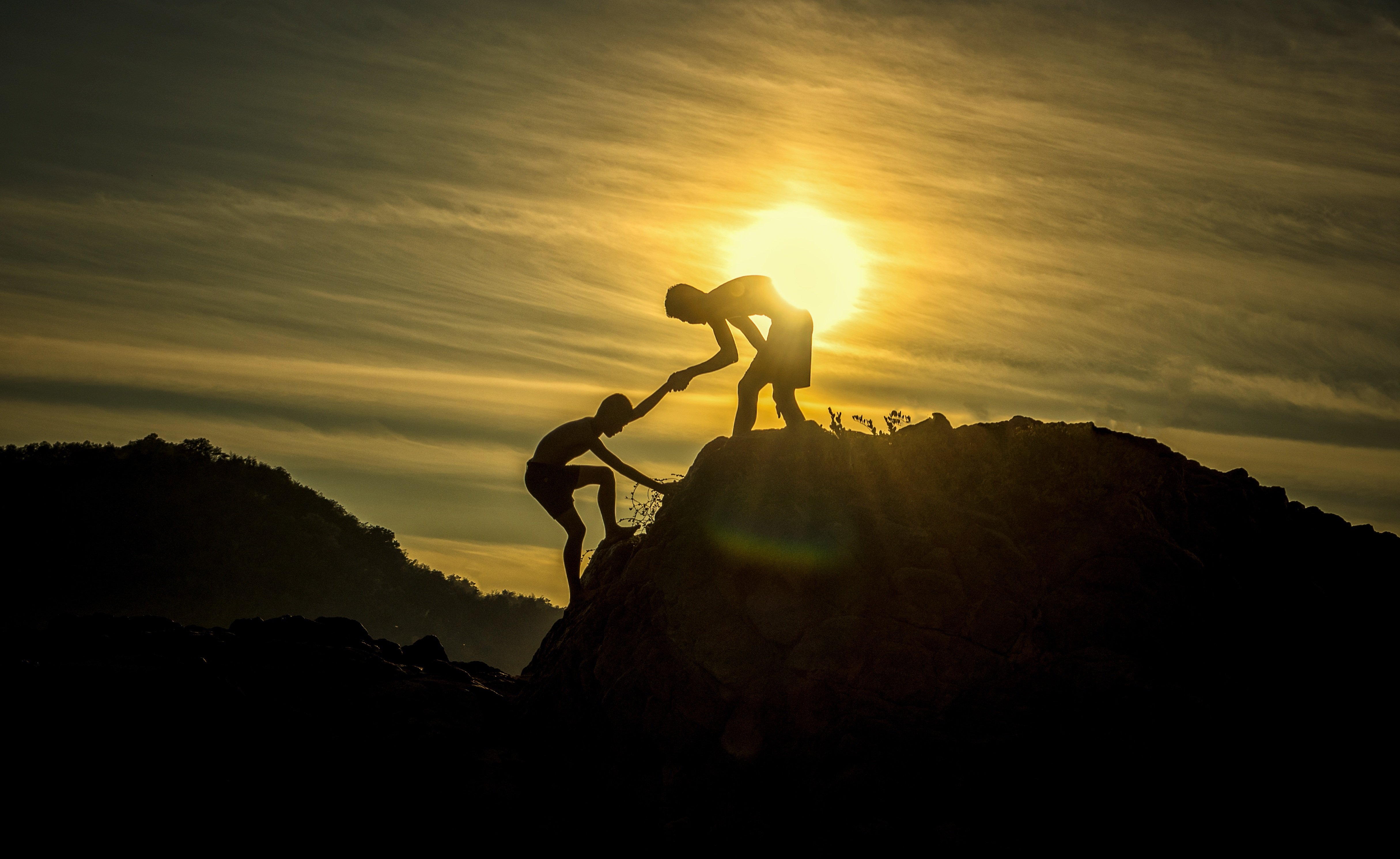 Two climbers helping each other up a peak at sunset.