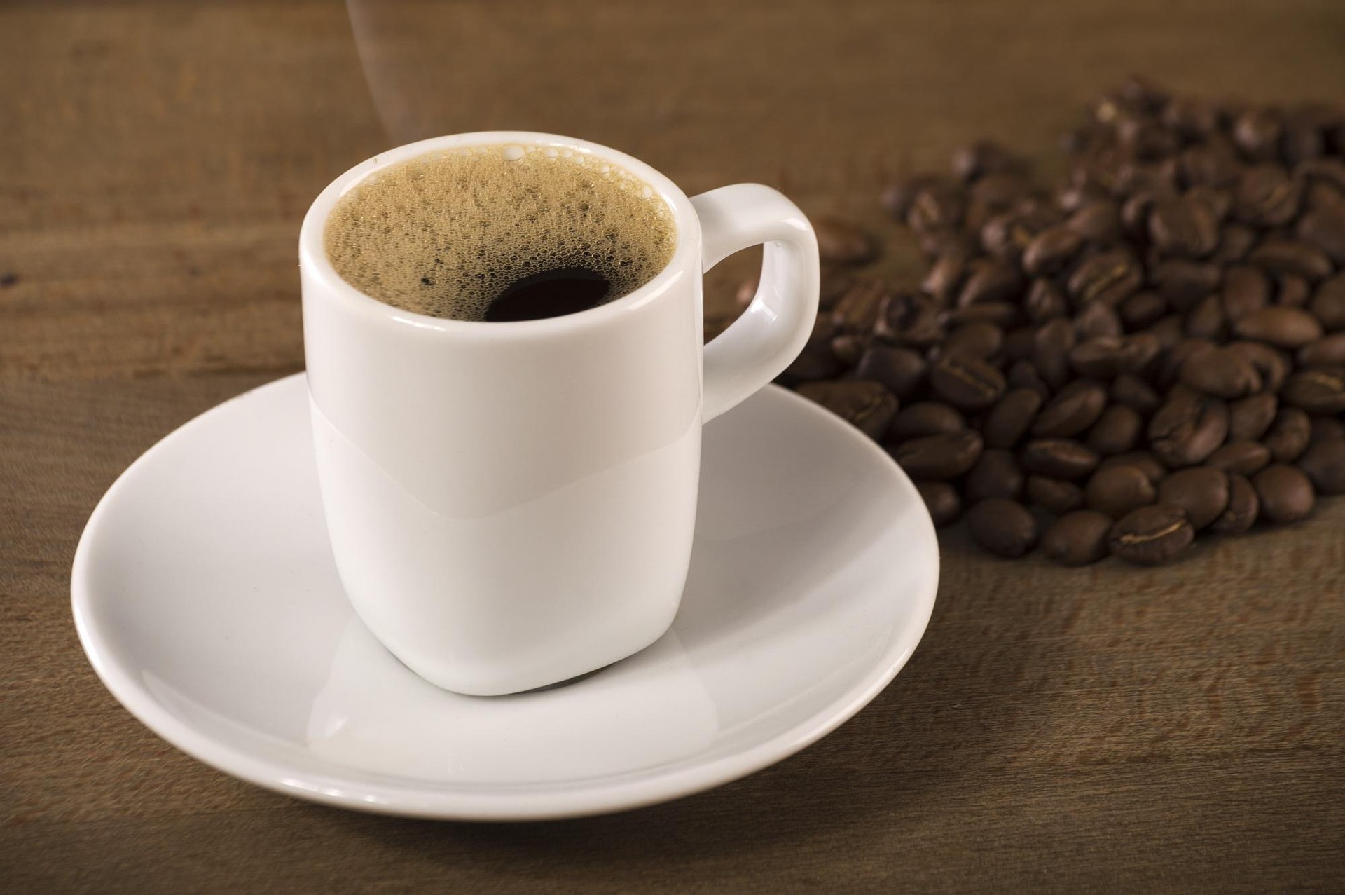 An espresso cup beside coffee beans on a wooden table.